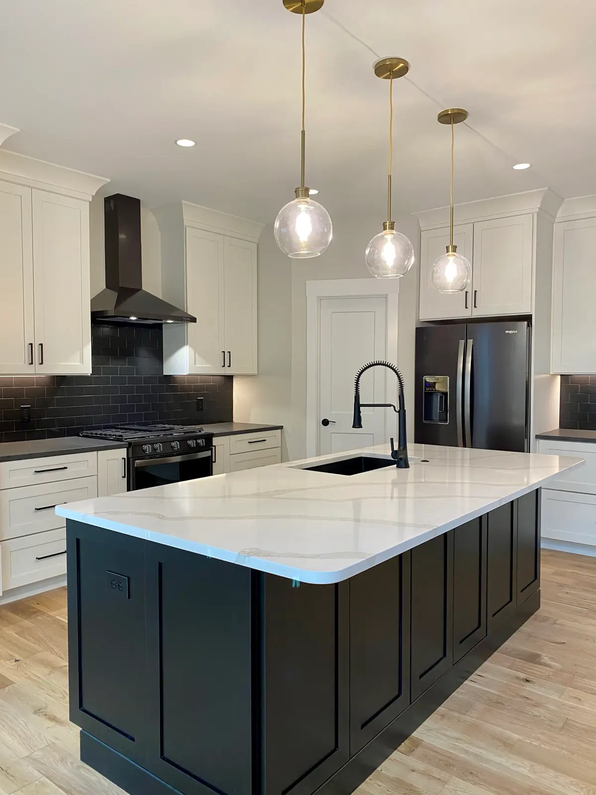 White kitchen with black island, black subway tile and brass globe pendants