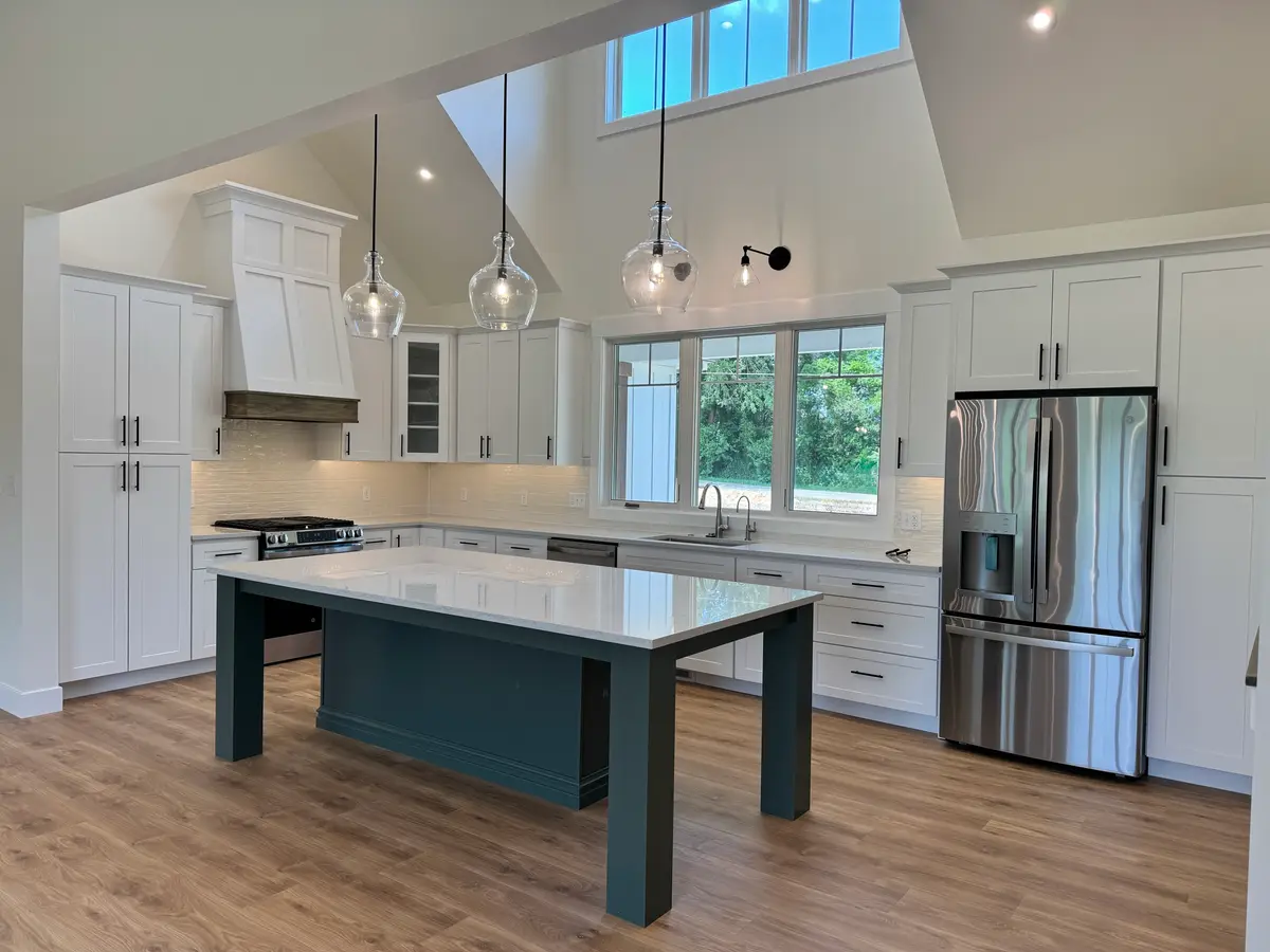 White vaulted kitchen with dark green island and glass pendant lights
