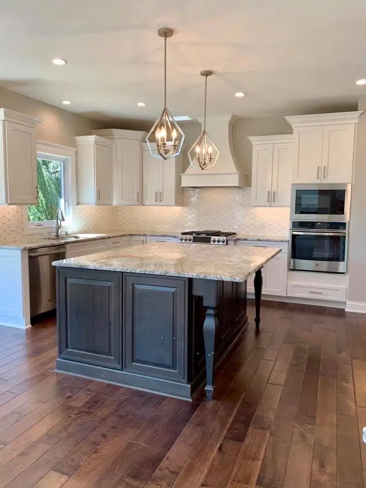 White kitchen with dark gray island on turned legs and geometric pendants