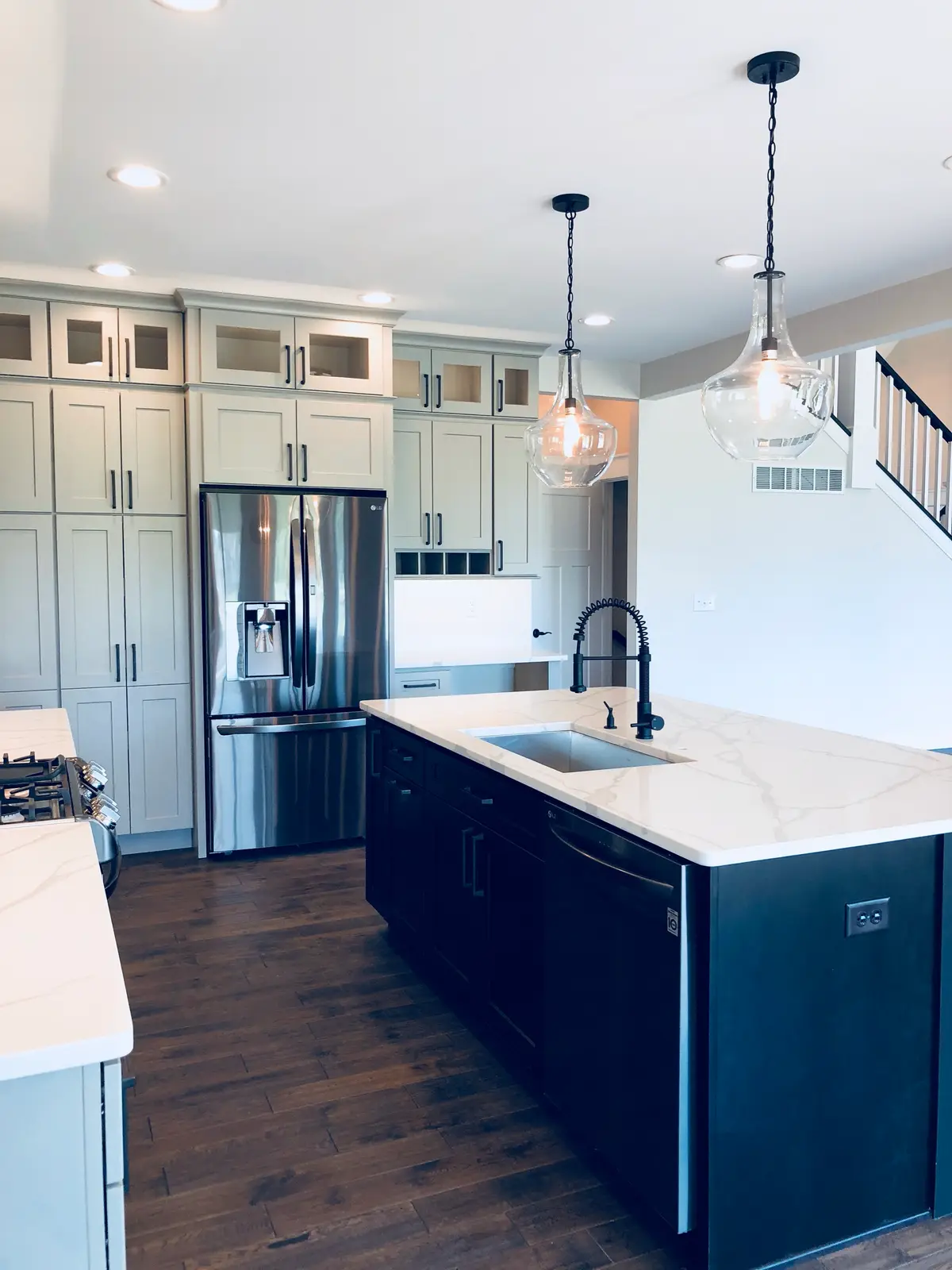 Gray shaker kitchen with dark island, marble-look quartz and glass pendants
