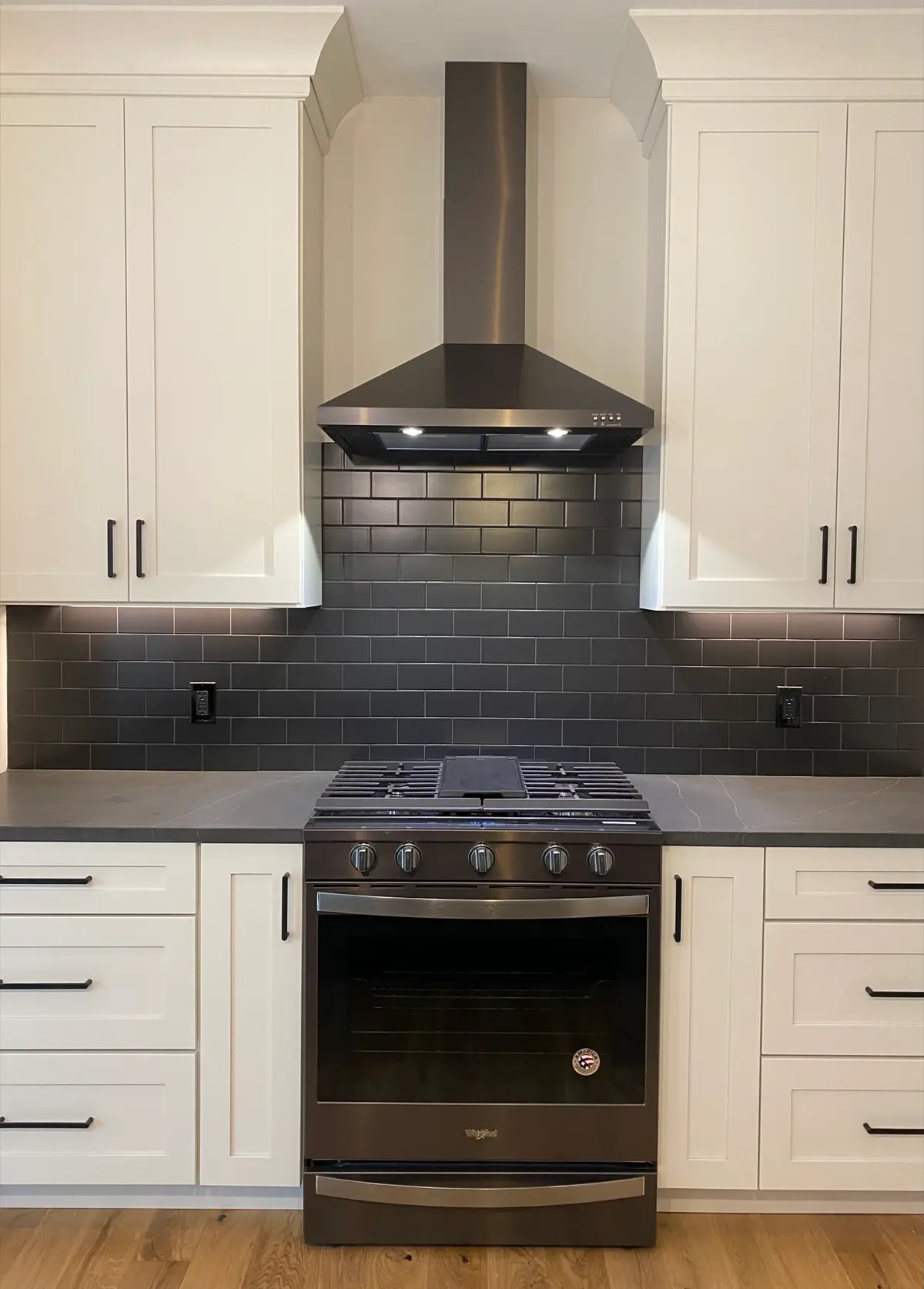 Black stainless chimney range hood over a gas range with charcoal subway tile
