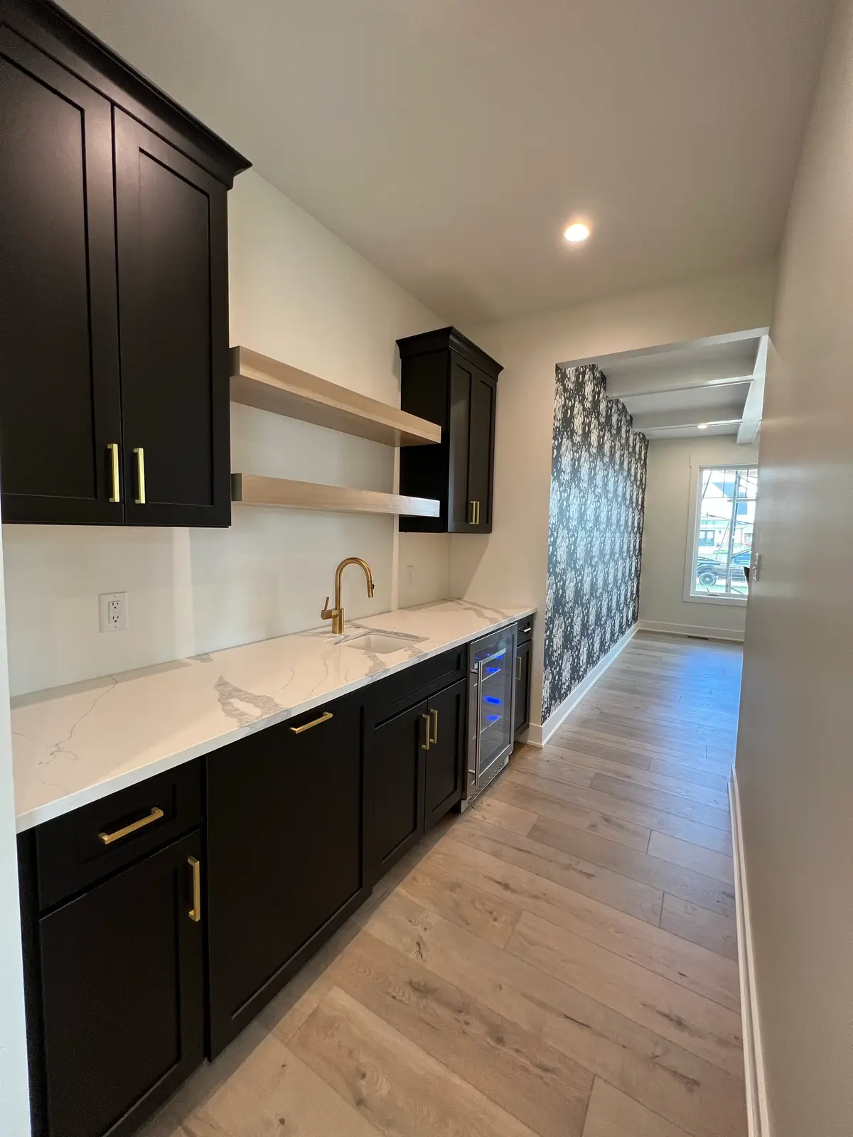 Butler's pantry with black cabinets, brass faucet and floating oak shelves