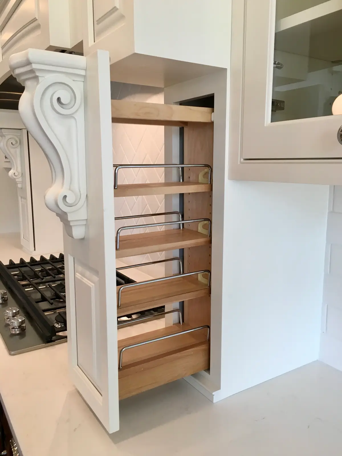 Pull-out spice rack beside the gas cooktop with a carved white corbel