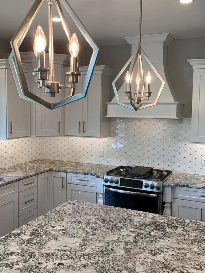 Geometric pendants over a granite island with white range hood and diamond tile