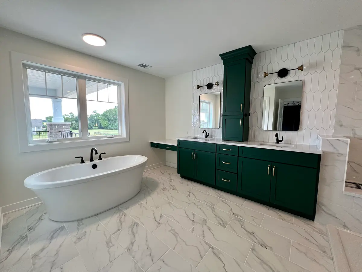 Master bath with freestanding tub, window and dark green double vanity