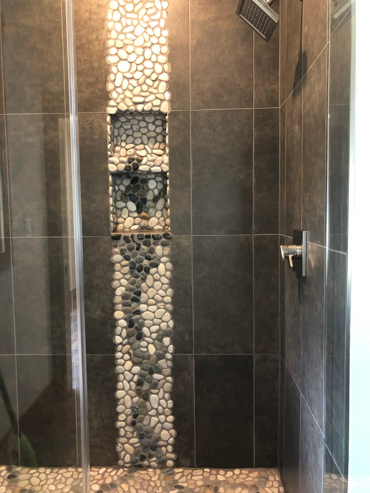 Walk-in shower with charcoal tile, pebble accent strip and inset niches