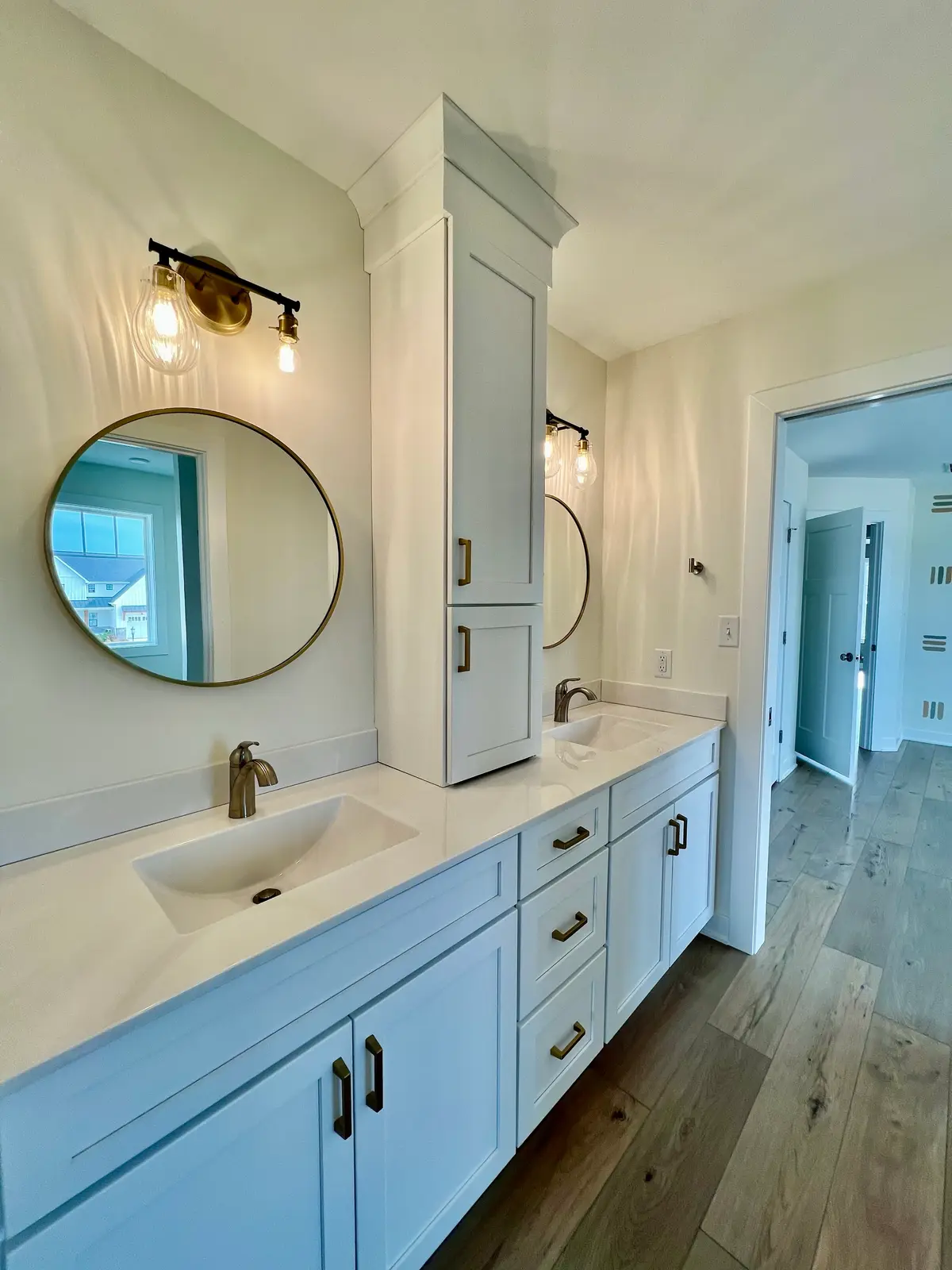 White double vanity with round brass mirrors and center linen tower