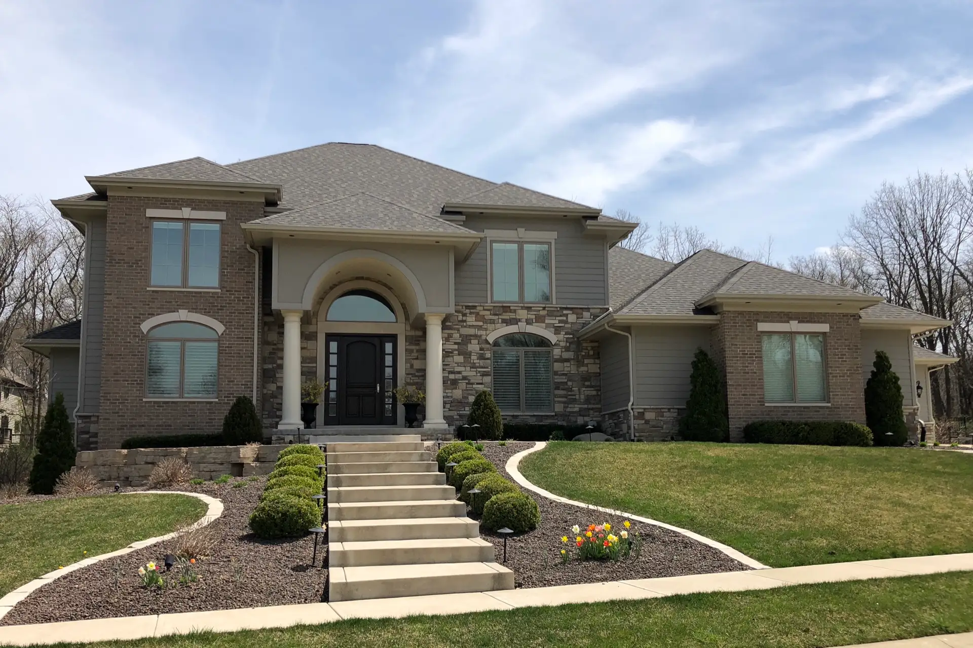 Two-story brick and stucco home with arched entry and landscaped front steps