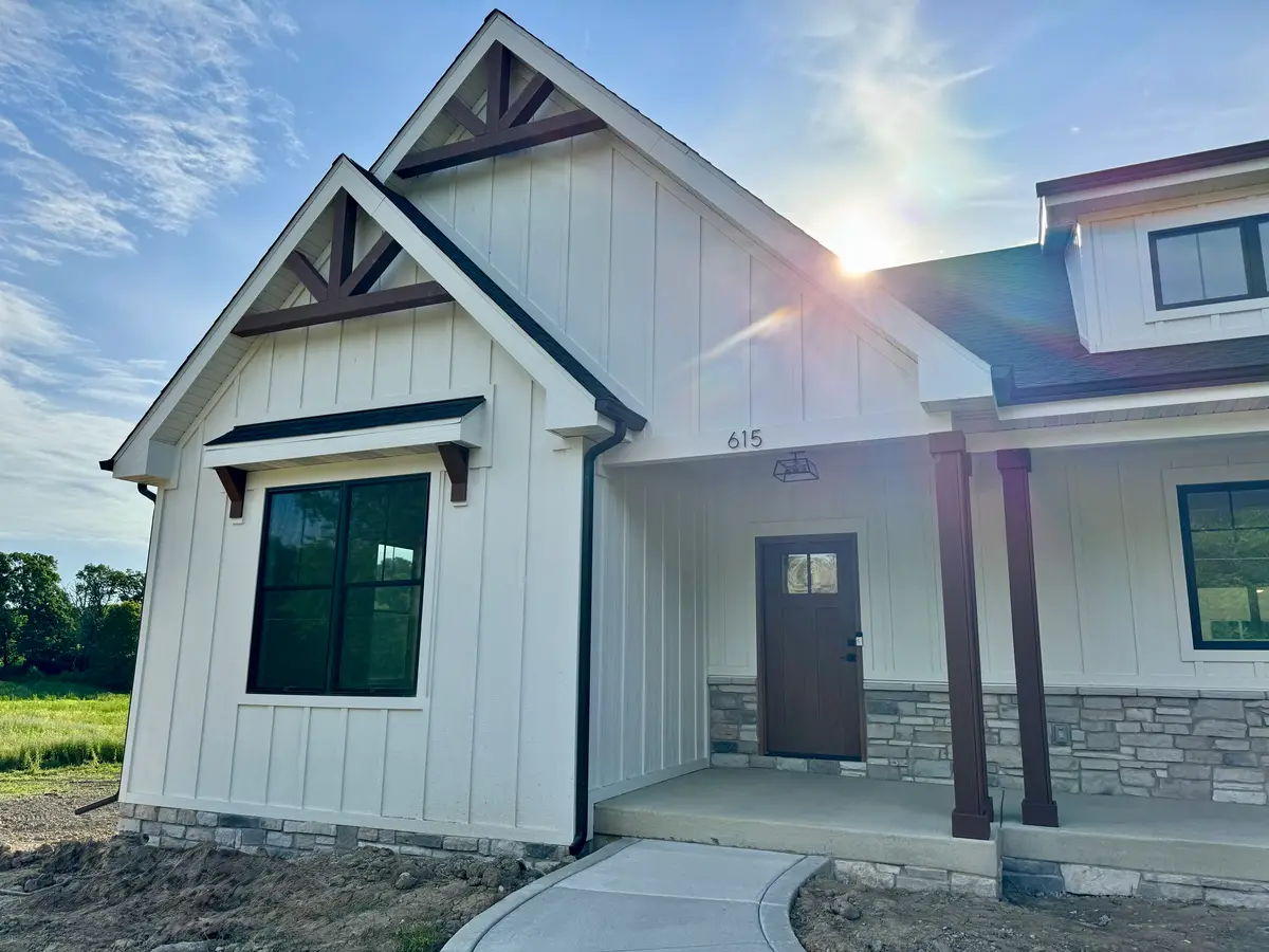 White board-and-batten farmhouse entry with gable brackets and stone wainscot