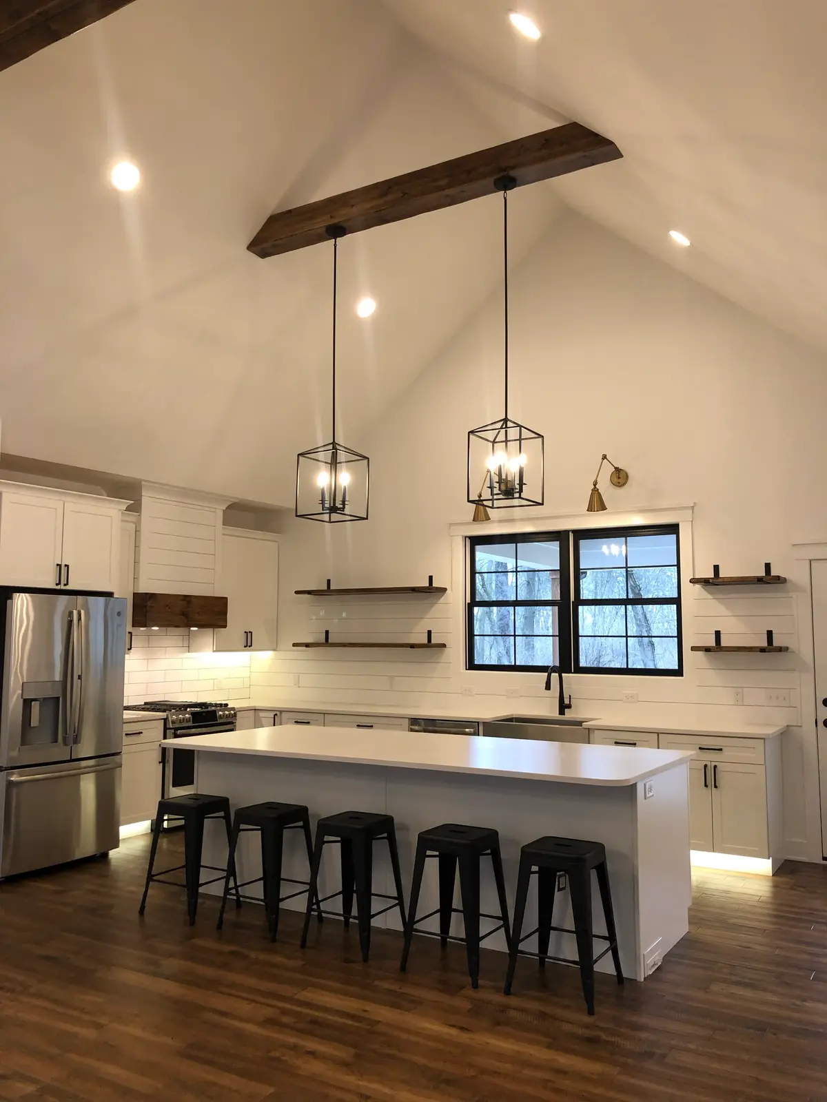 Vaulted white farmhouse kitchen with wood beam, cage pendants and island seating