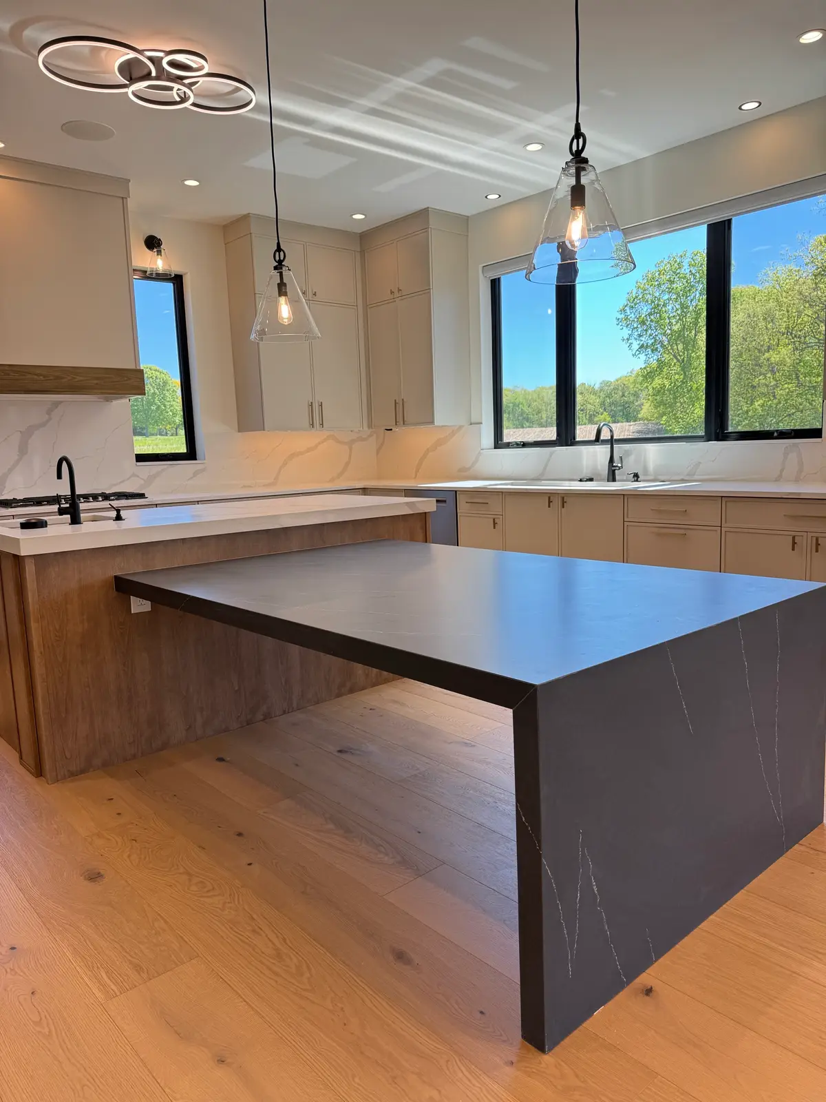 Modern kitchen with black quartz waterfall island and glass pendants