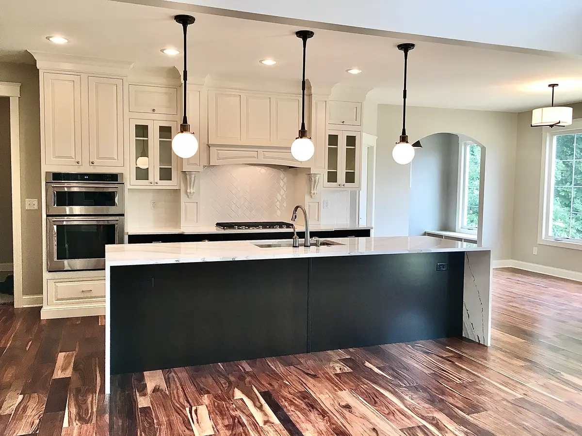 White kitchen with black waterfall island, globe pendants and hardwood floors