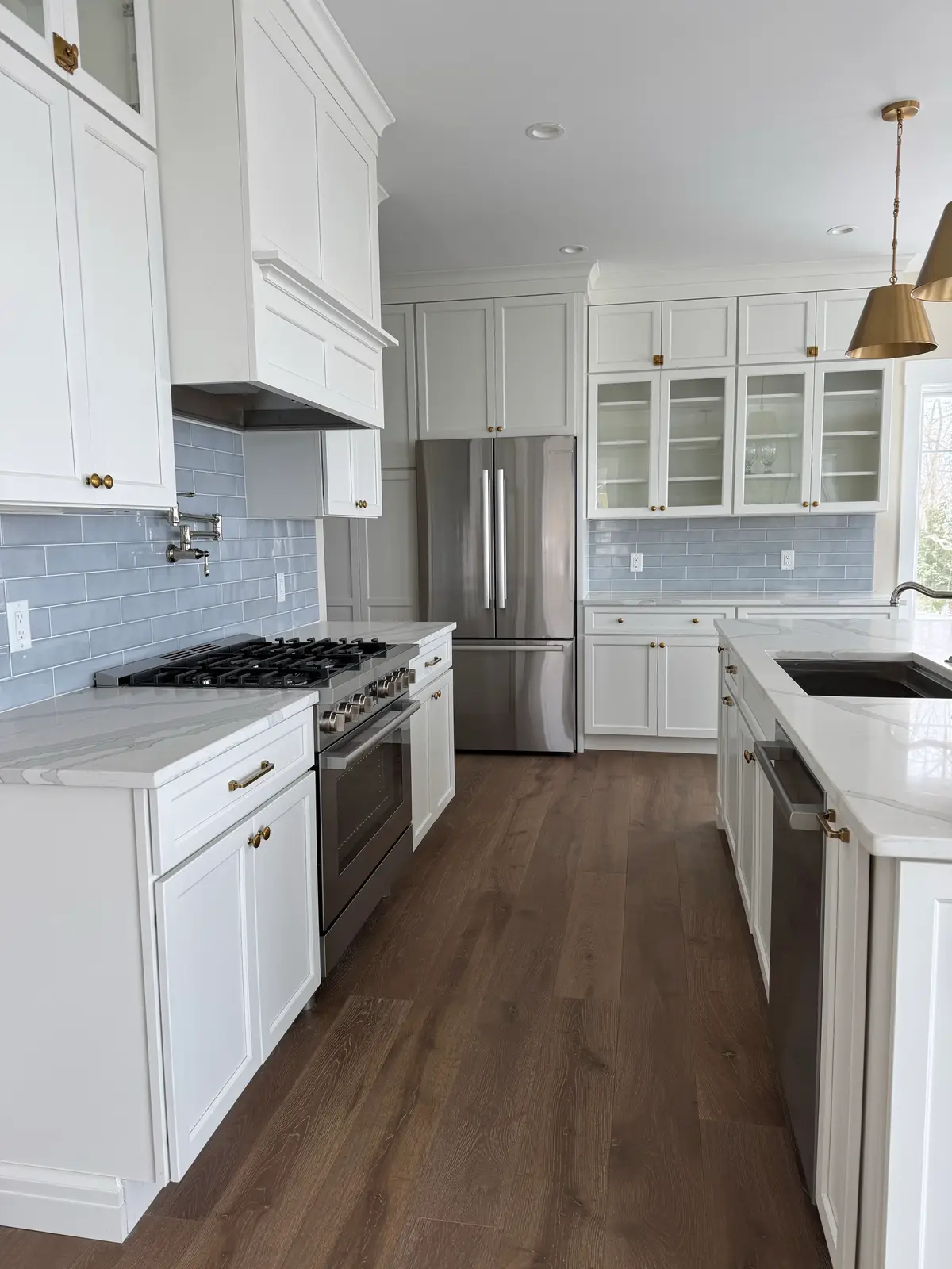 White kitchen with pale blue subway tile, brass hardware and glass-front cabinets