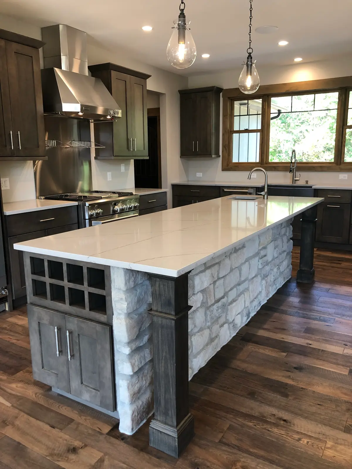 Stone-wrapped kitchen island with white quartz top and glass pendants